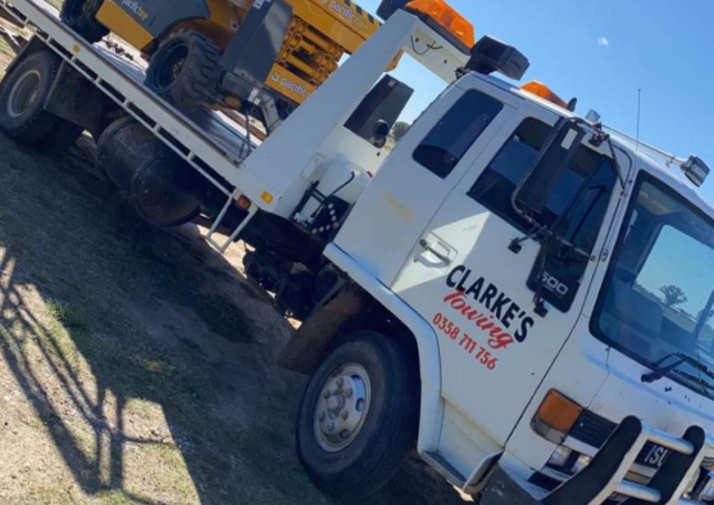 Yellow scissor lift loaded on the Clarke's Towing tray on a rural property
