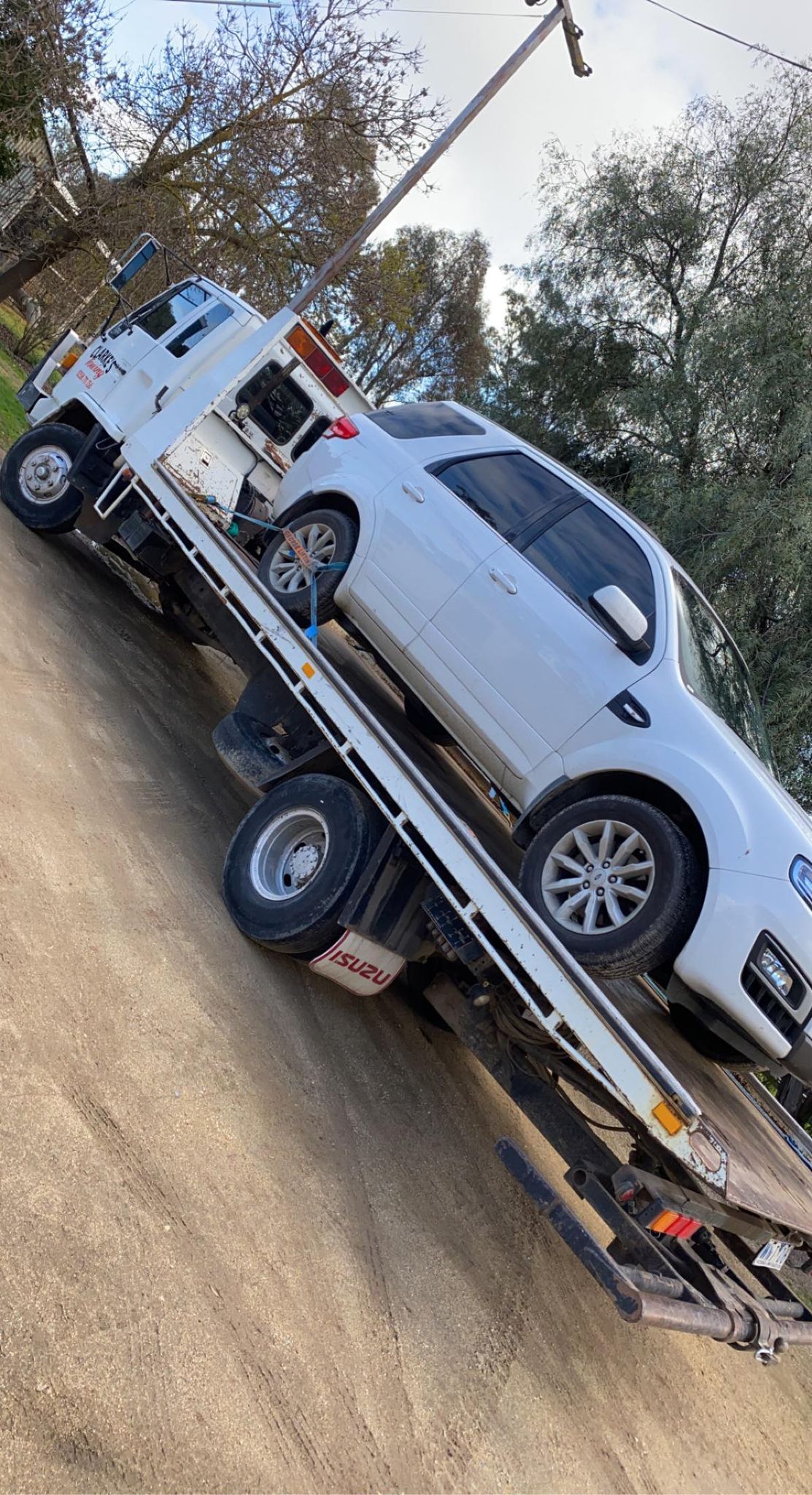 Clarke's Towing flatbed carrying a white SUV on a gravel road