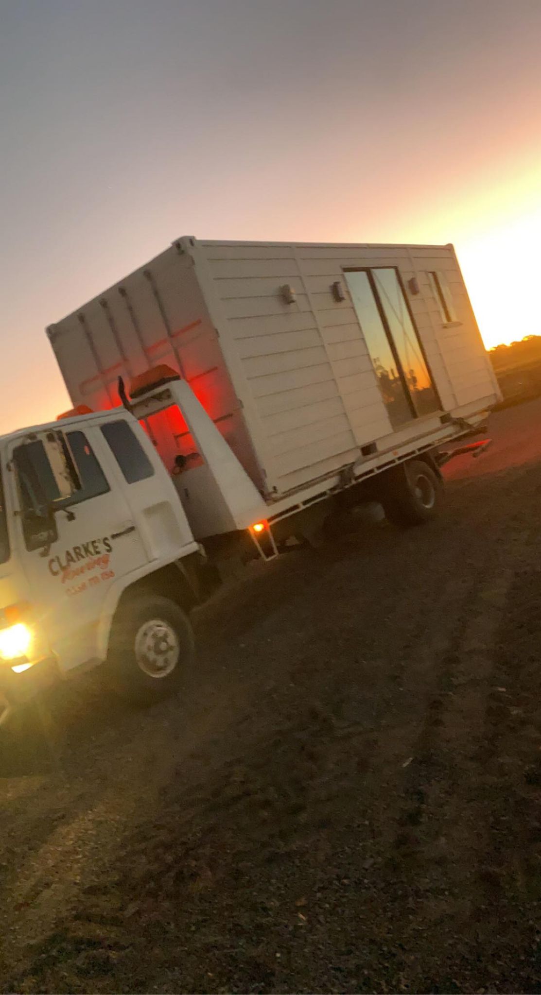 Clarke's Towing truck carrying a small transportable cabin at sunset