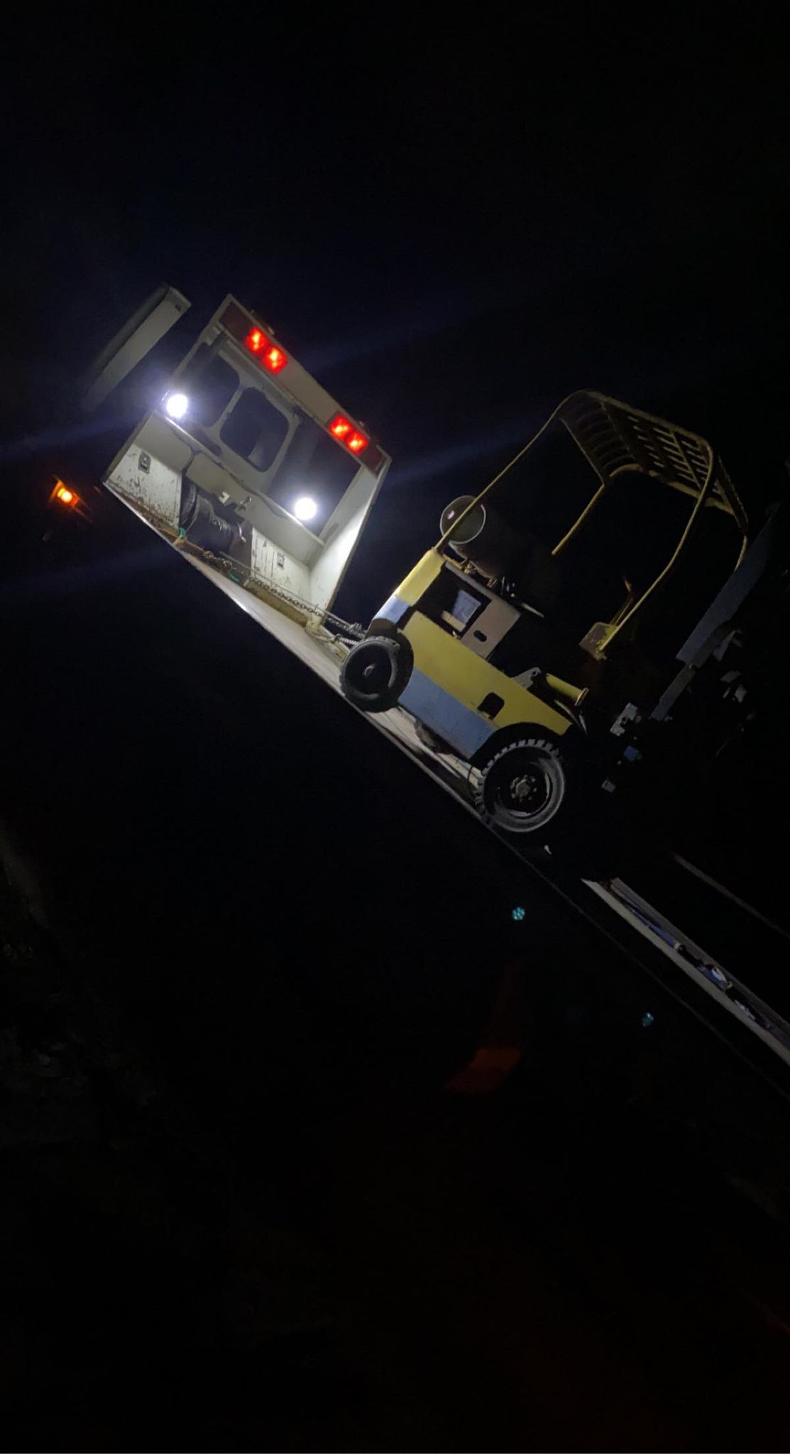 A forklift being loaded onto the Clarke's Towing tray at night under work lights